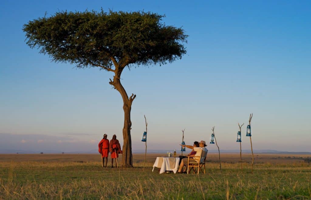 Sundowner drinks under an acacia tree overlooking the Masai Mara